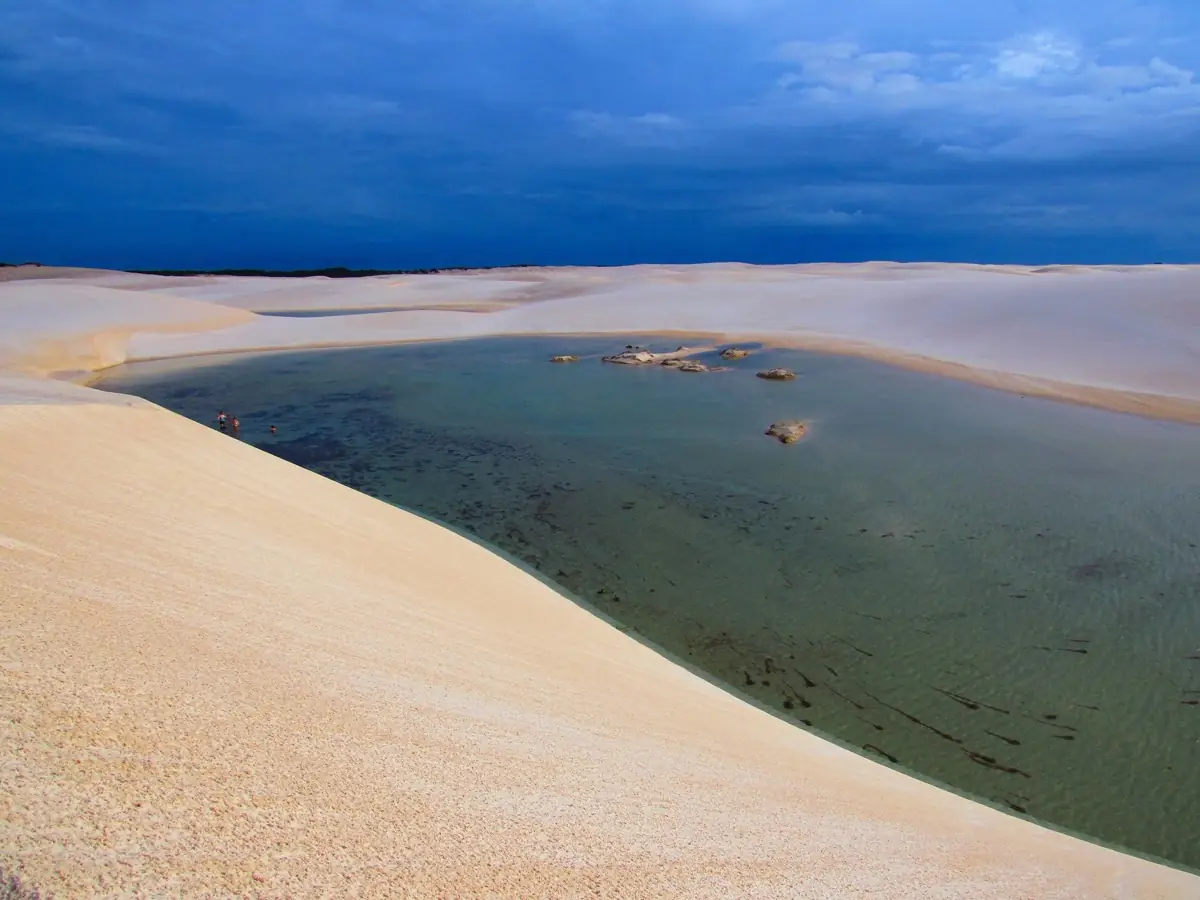 Crista de duna descendo para uma lagoa larga nos Lençóis Maranhenses